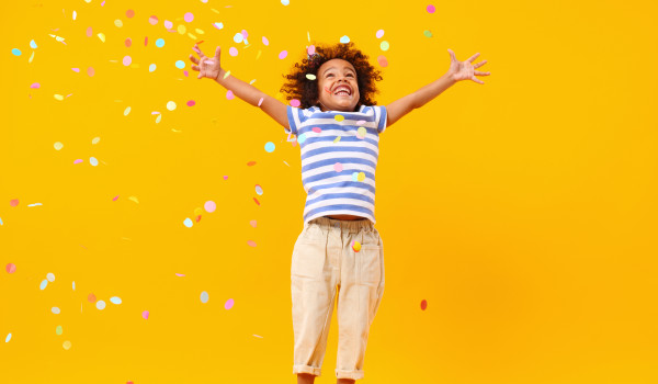 Young girl jumping with confetti and yellow background
