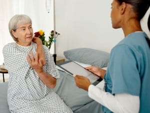 a picture of a female healthcare worker on an electronic device with an elderly female patient sat on a bed.