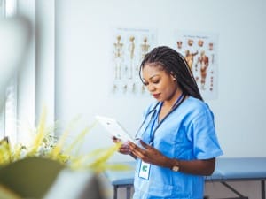 A picture of a female healthcare worker in blue scrubs looking down an an electronic device.
