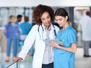 2 female healthcare workers in a hospital setting looking at an electronic device.