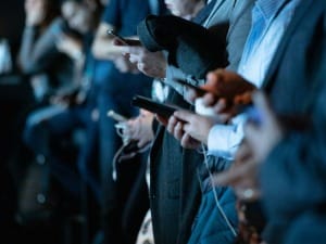 A picture showing multiple people viewing social media on their mobile devices.