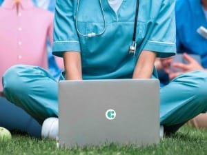 A picture of a healthcare professional sat on grass with a System C laptop.