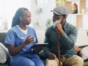 A picture of a female healthcare worker sat with an electronic device, talking to a male patient.