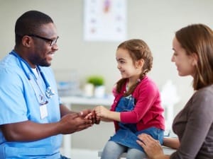 A picture of a male healthcare worker interacting with a child and her guardian.