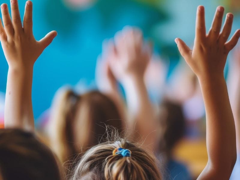 school children holding hands up in class room setting education